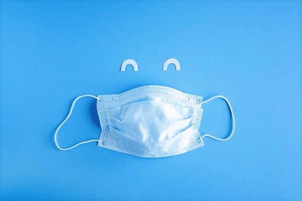Disposable medical mask on blue background with white paper eyes. Smiling cut off face with medical mask. Stop the spread of coronavirus, self-defense. Copy space